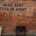 A sign on a brick wall that references debt and the potential impact on revenue