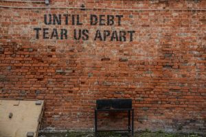 A sign on a brick wall that references debt and the potential impact on revenue